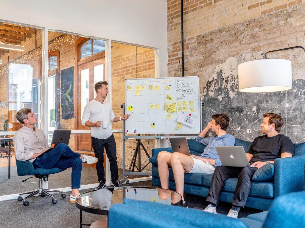 4 men sat around a whiteboard with sticky notes on