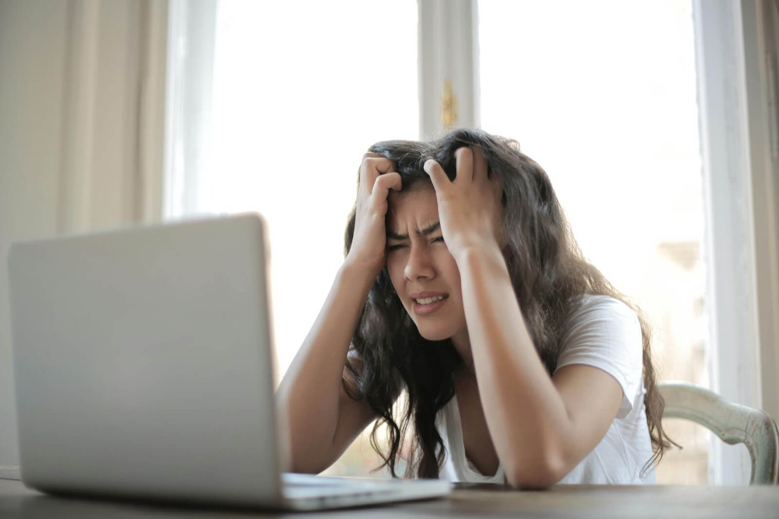 Woman with brown hair with her hands on her head looking very stressed.